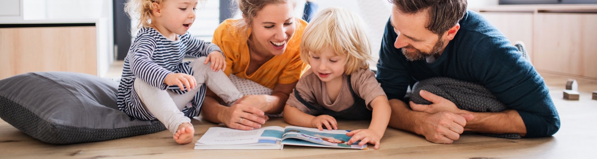 Jong gezin met twee kleine kinderen binnenshuis in de slaapkamer die een boek lezen.