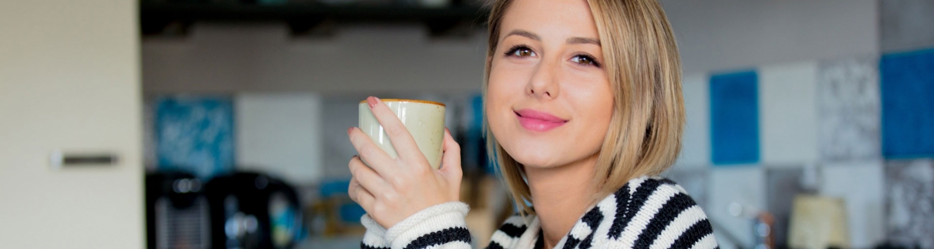 Jonge dame in trui zit aan tafel tijdens het ontbijt met een kop koffie in de keuken.
